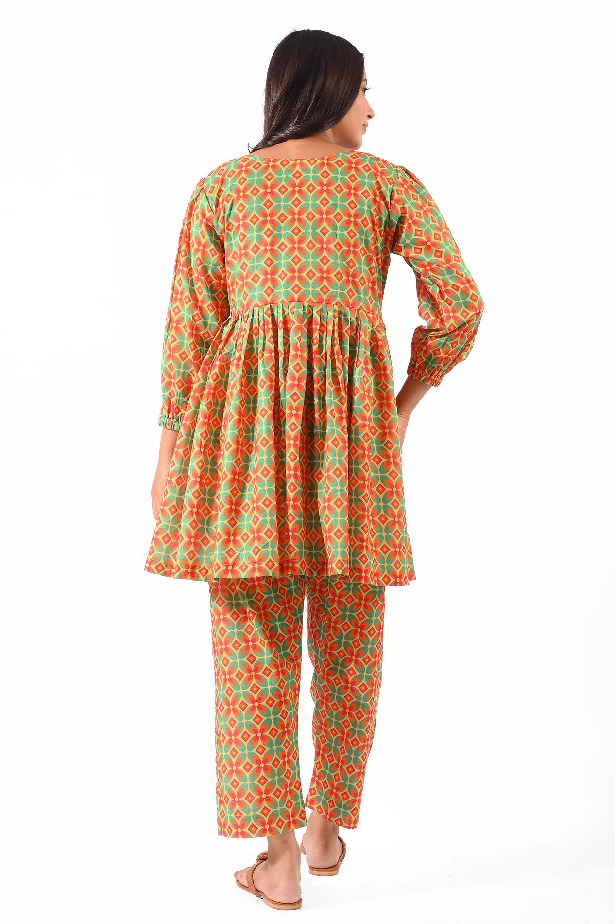 A back view of a model wearing a vibrant orange and green dress with a matching patterned straight pant. The dress features a gathered waistline and puffed sleeves, styled with flat sandals BOLDSTEP BOLDSTEP.PK