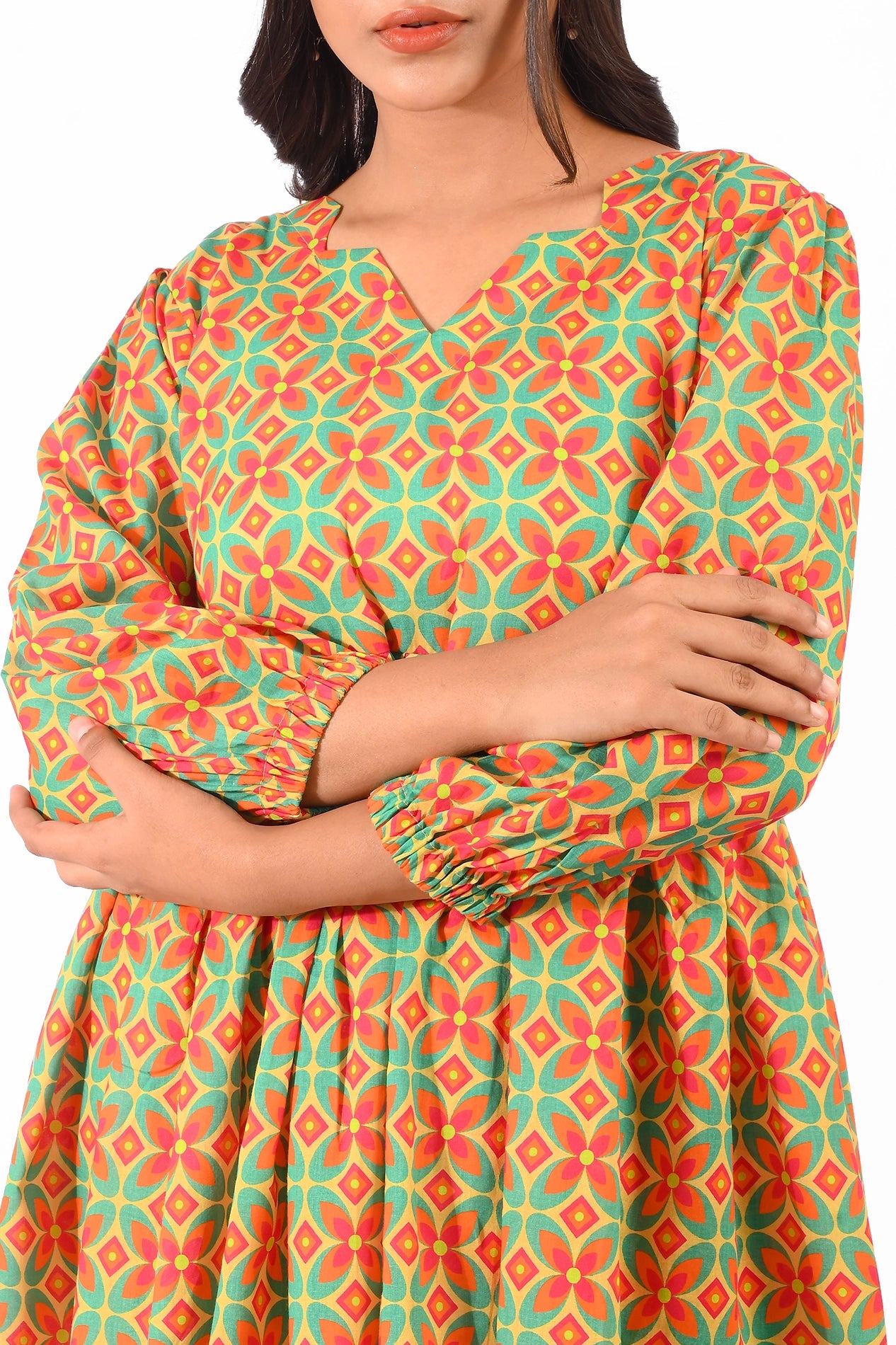 A close-up of the model’s upper body wearing a colorful orange and green patterned dress with a V-neckline, puffed sleeves, and gathered waistline. The design highlights the intricate pattern details BOLDSTEP BOLDSTEP.PK