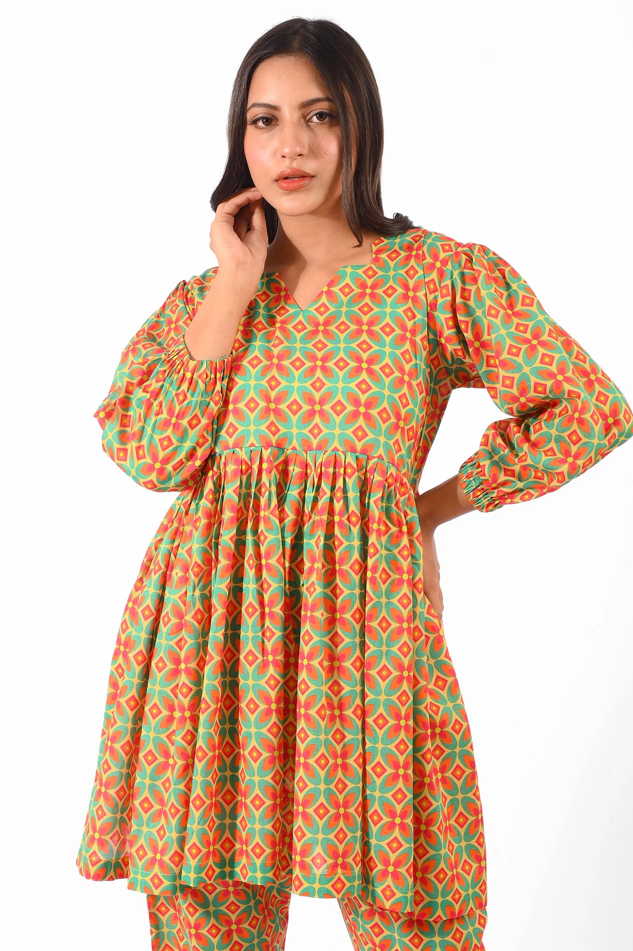 A medium close-up of a model showcasing a vibrant orange and green patterned dress with a V-neckline and puffed sleeves. The outfit emphasizes the detailed geometric pattern and casual flow of the fabric BOLDSTEP BOLDSTEP.PK
