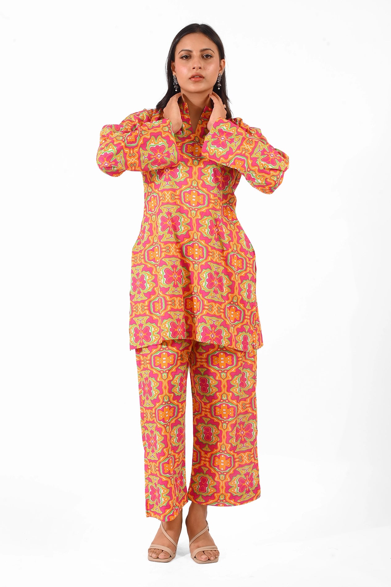 A front-facing view of a model wearing a vibrant kurta and trouser set with colorful geometric and floral patterns in shades of pink, orange, and green, paired with beige heels and statement earrings BOLDSTEP BOLDSTEP.PK