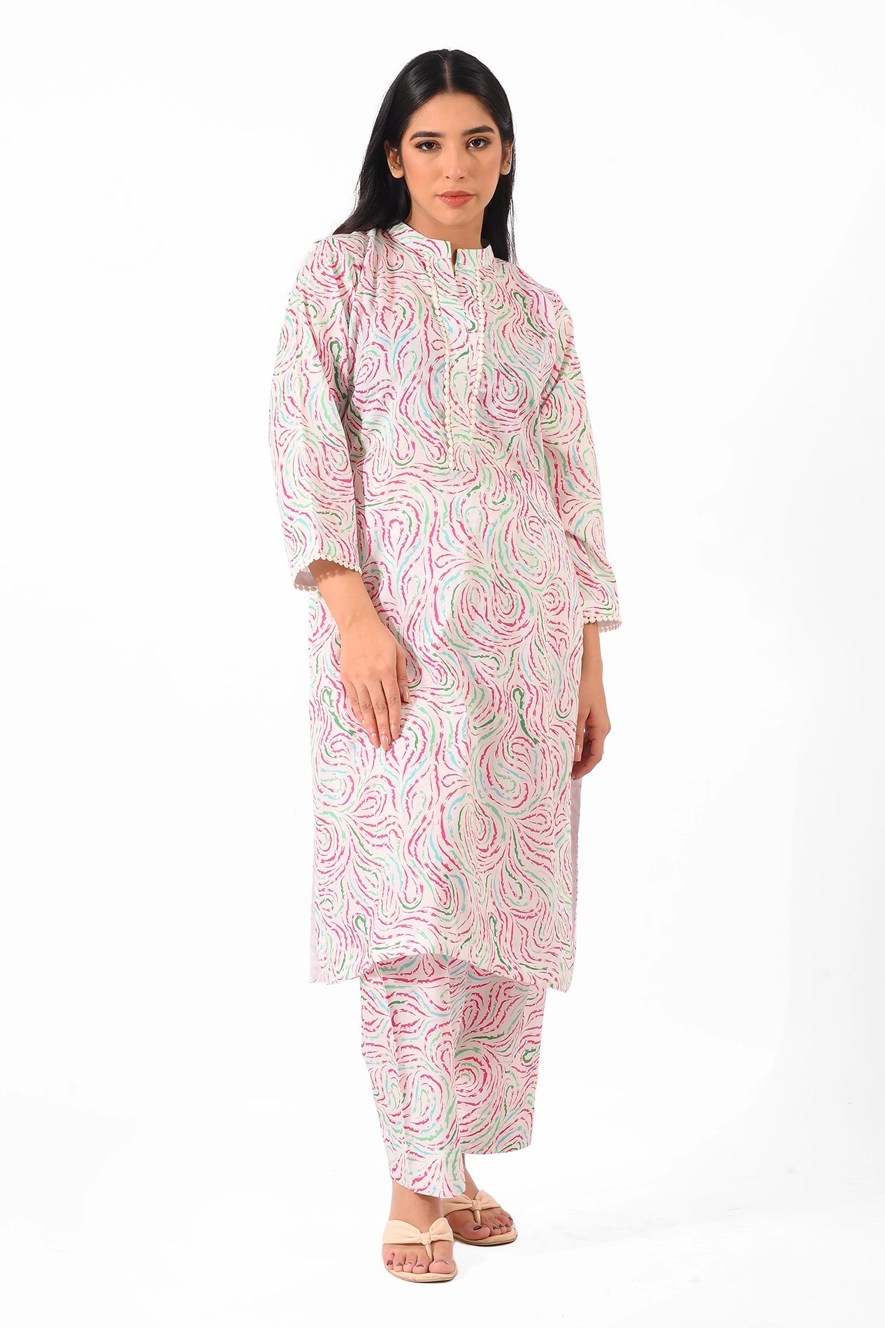A woman modeling a long, pastel-patterned kurta set with abstract pink and green swirls. She stands gracefully, showcasing the straight kurta and matching trousers paired with simple nude sandals BOLDSTEP BOLDSTEP.PK