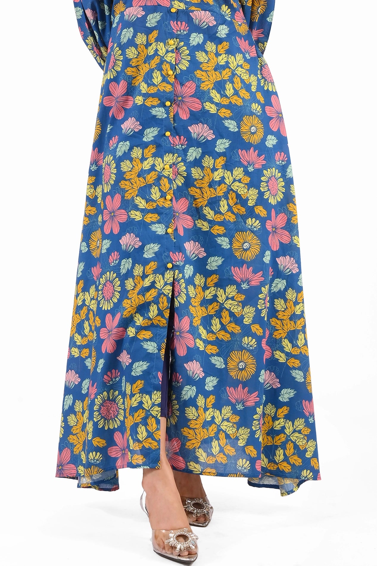 Close-up view of the blue maxi dress, highlighting the colorful floral patterns and a subtle front slit detail at the bottom. The dress is styled with sparkling silver heels. BOLDSTEP BOLDSTEP.PK