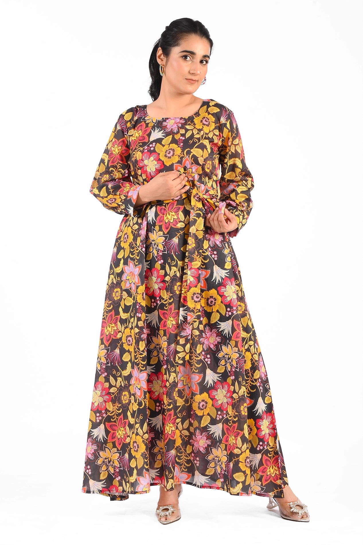 Full-length floral printed black dress with vibrant yellow, pink, and red flower patterns, accessorized with a matching belt and elegant silver heels. The dress features long sleeves and a round neckline. BOLDSTEP BOLDSTEP.PK