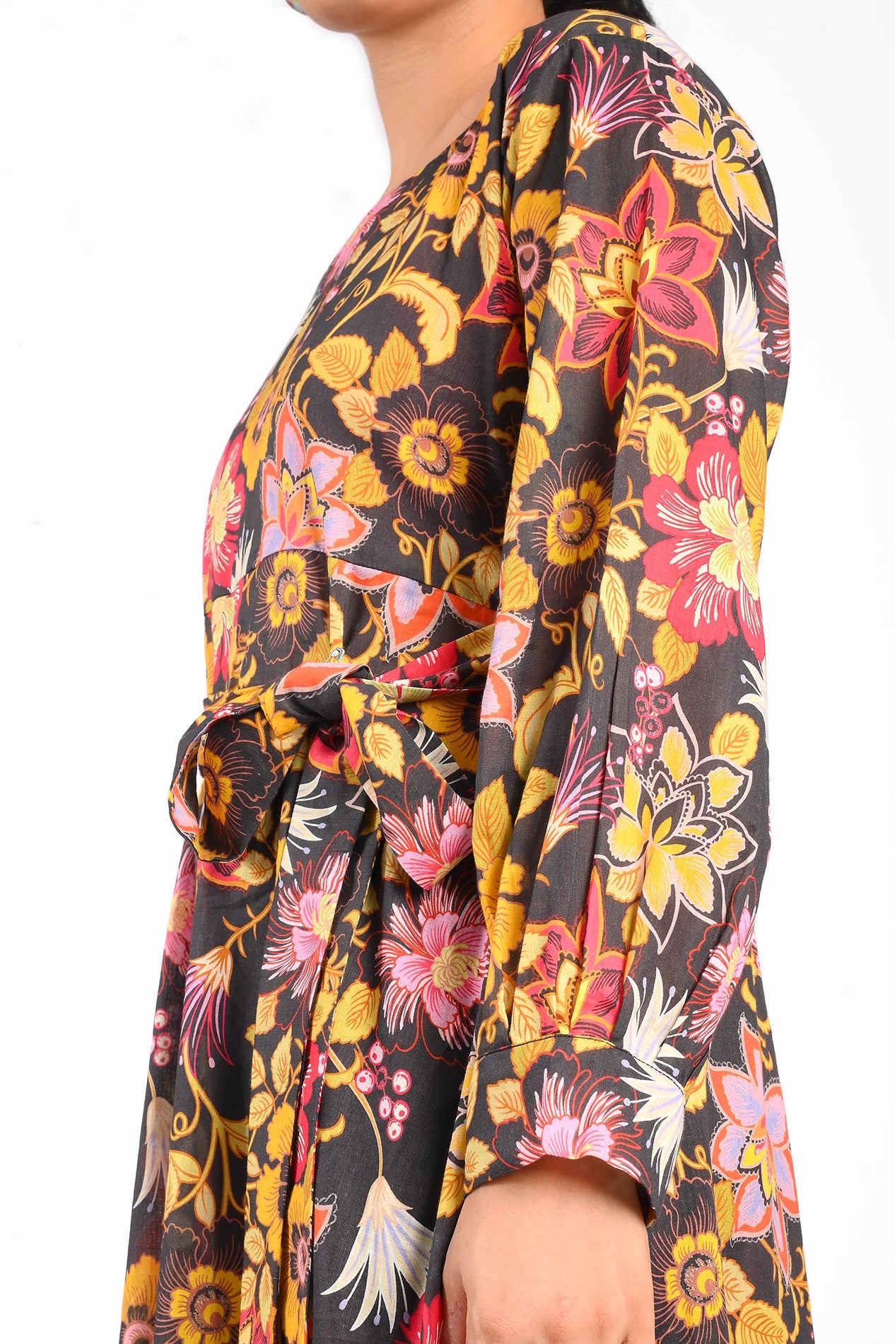 Model wearing a floral black maxi dress with vibrant multicolored flower patterns, showcasing its flowy fit and tied belt. The dress features long sleeves and a full skirt. BOLDSTEP BOLDSTEP.PK