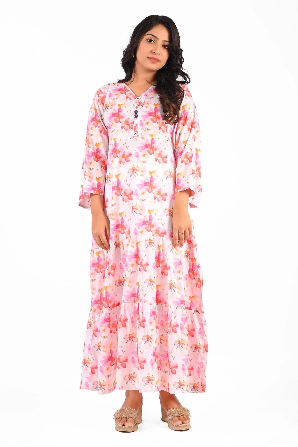 A model wearing a pink floral maxi dress with a tiered design, featuring long bell sleeves and a V-neckline adorned with buttons, styled with beige wedge sandals. BOLDSTEP BOLDSTEP.PK