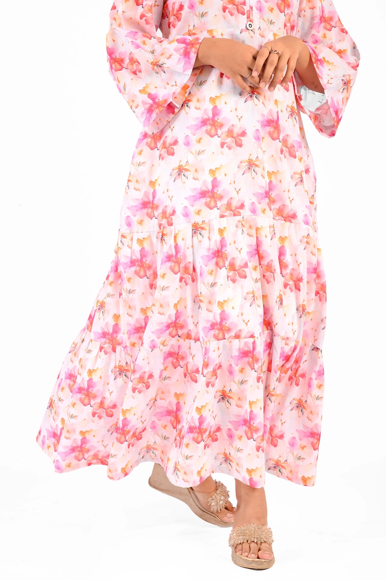 Zoomed-in view of the lower half of the pink floral maxi dress, emphasizing its tiered design and the intricate floral pattern, paired with beige wedge sandals. BOLDSTEP BOLDSTEP.PK
