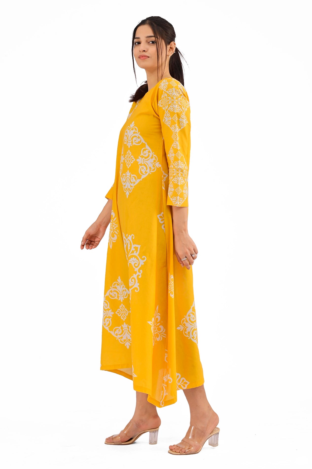 Side view of a yellow long dress with white decorative patterns. The model showcases the straight cut of the dress and its flowy design while holding her posture elegantly. BOLDSTEP BOLDSTEP.PK