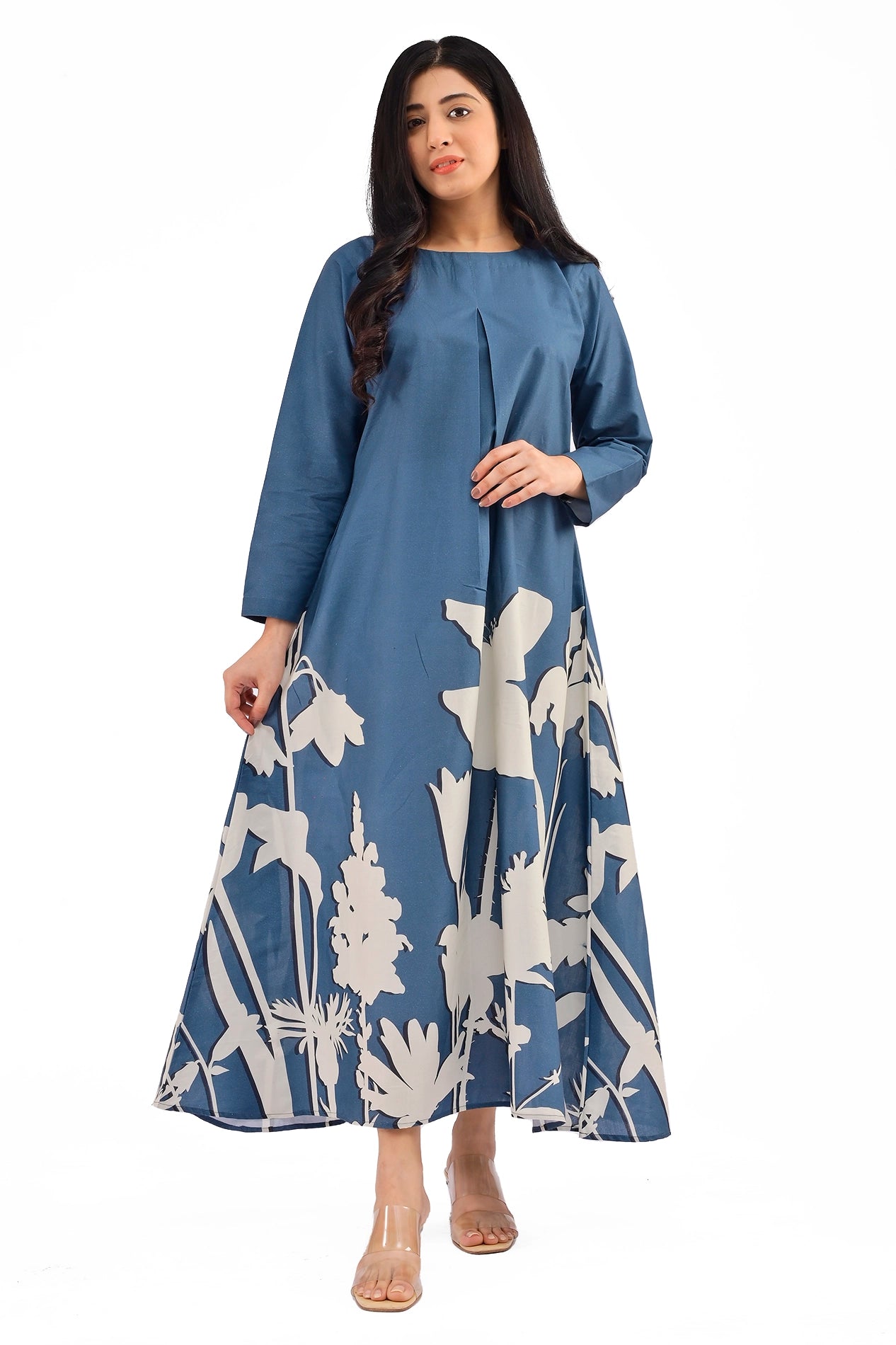 Model wearing a blue A-line dress with long sleeves and a round neckline, featuring white floral silhouette prints along the hem, paired with transparent heels. BOLDSTEP BOLDSTEP.PK