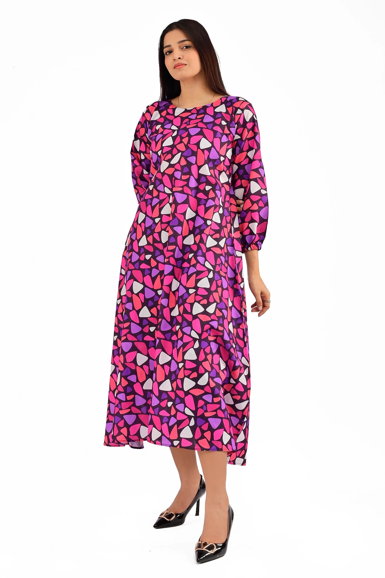 Woman wearing a vibrant mosaic-patterned dress in shades of pink, purple, and white with a round neckline and long elastic-cuffed sleeves, styled with black pointed heels. BOLDSTEP BOLDSTEP.PK