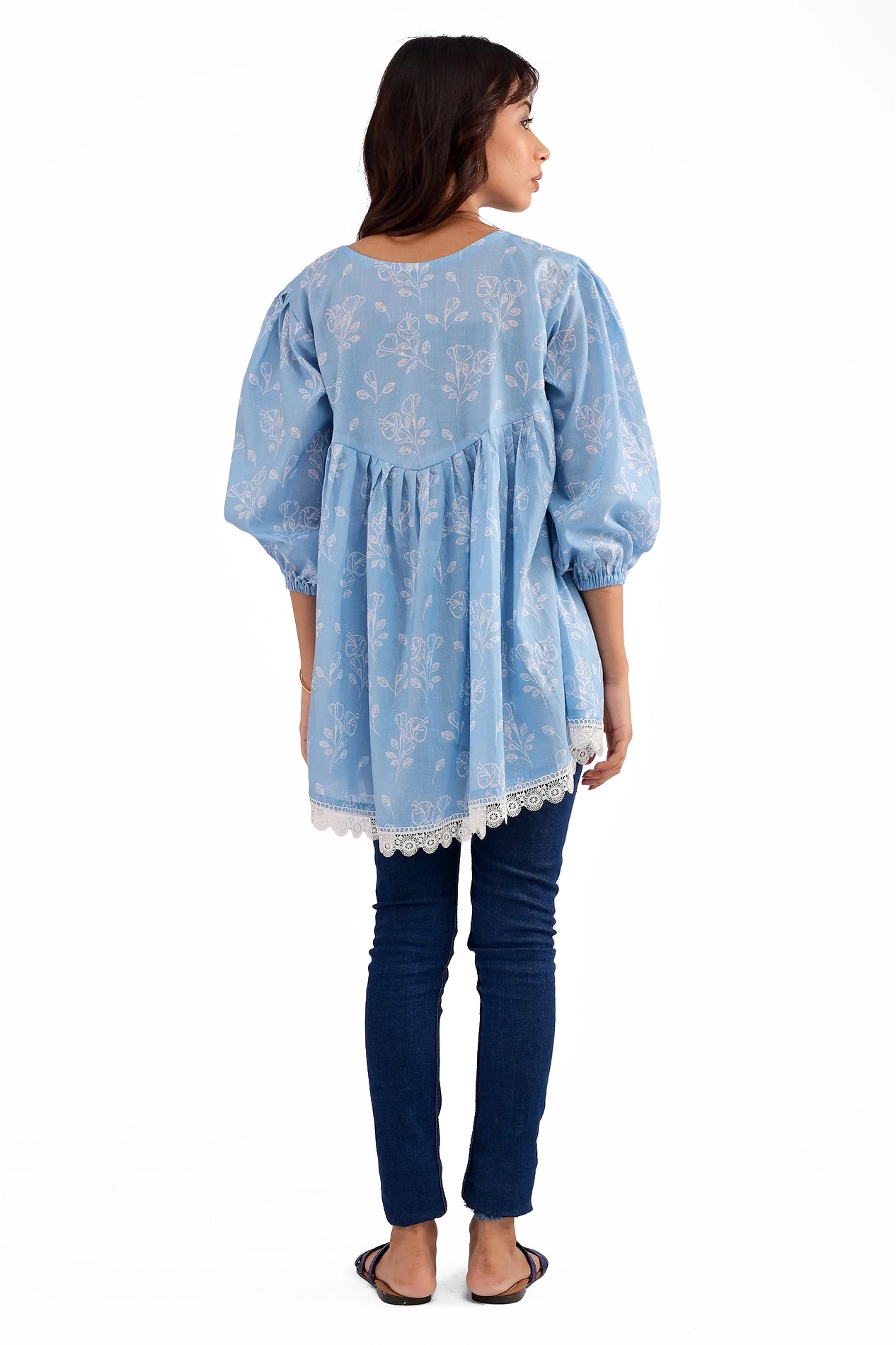 A back view of the tunic featuring a softly curved yoke with pleats flowing down to a relaxed fit, completed with intricate lace trimming at the hem