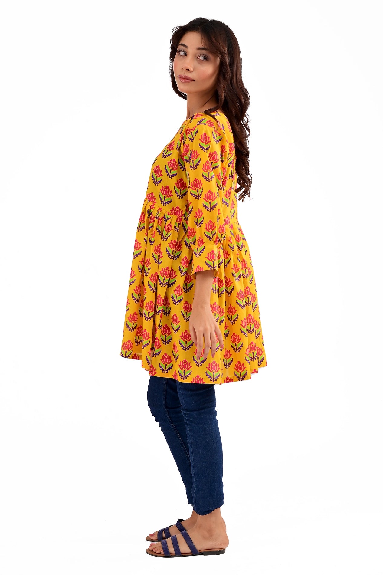 Side profile of a model in a yellow floral tunic, displaying its flowy silhouette and gathered waist, styled with fitted jeans and open-toe sandals