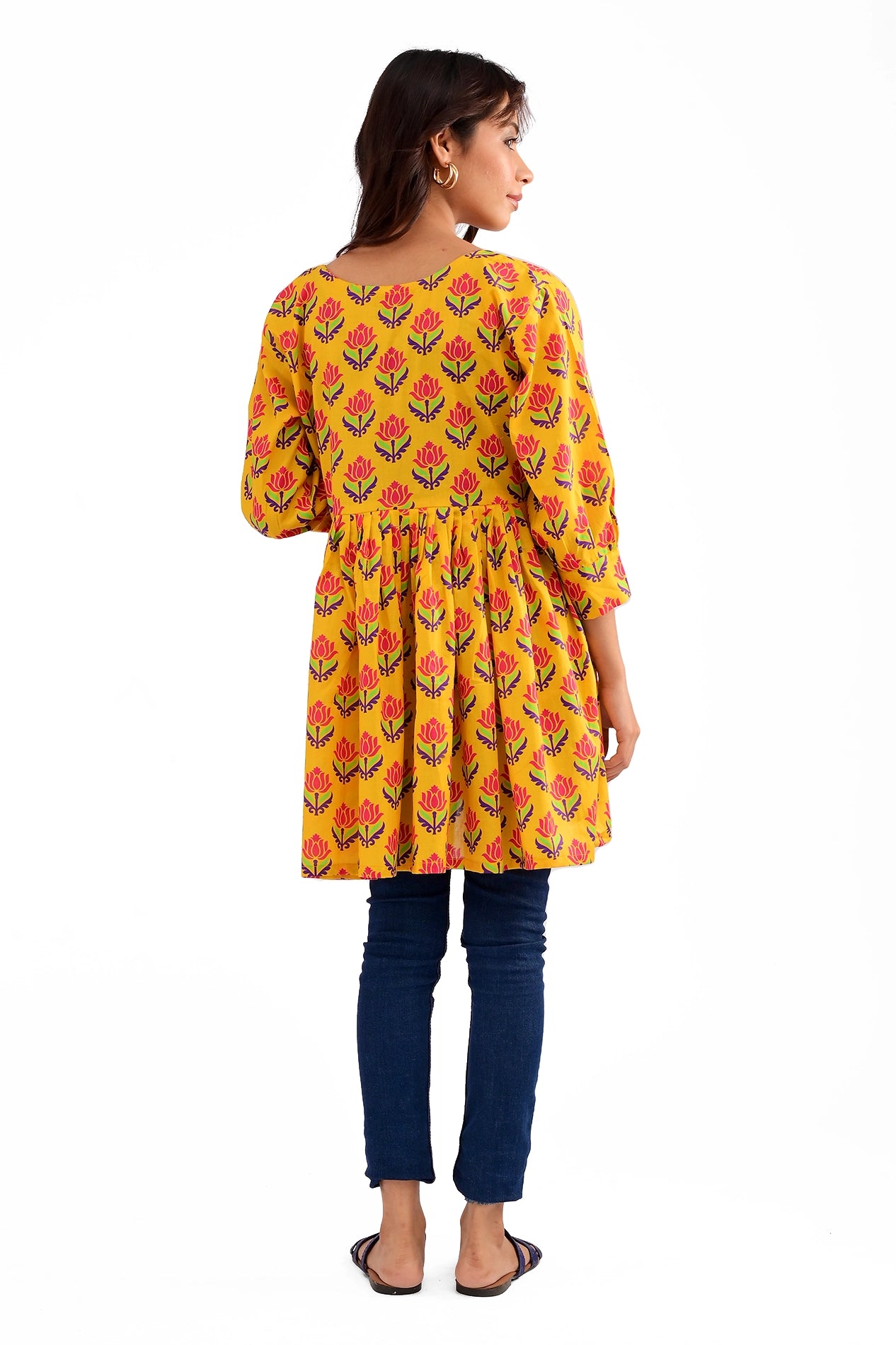 Rear view of the yellow floral tunic, displaying its pleated design and slightly curved hem, styled with dark blue jeans