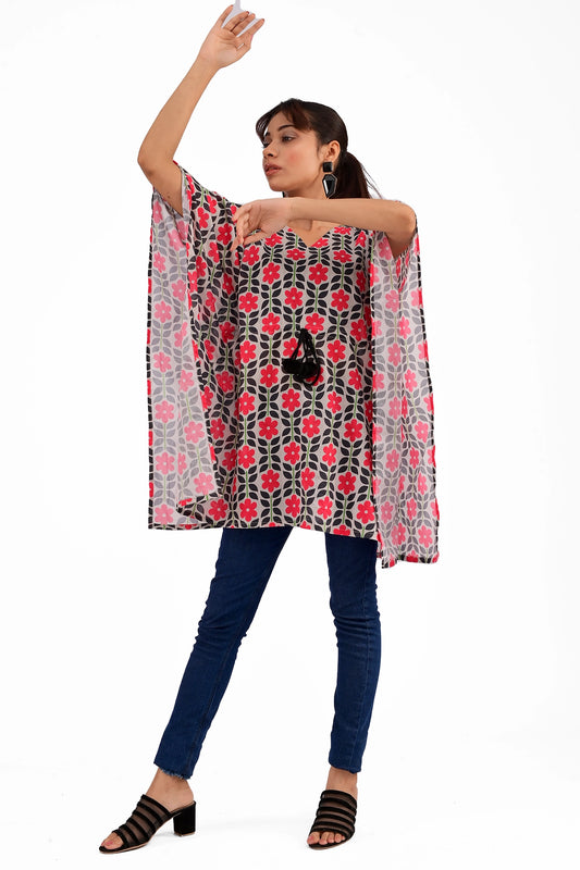 A model wearing a black and red floral printed kaftan-style tunic with loose-fitting sleeves, paired with blue jeans and black heels, posing against a white background
