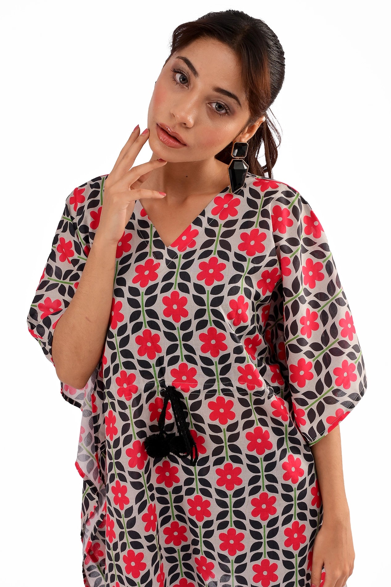 A close-up shot of a model wearing a floral printed kaftan tunic with a V-neck, accessorized with black geometric earrings