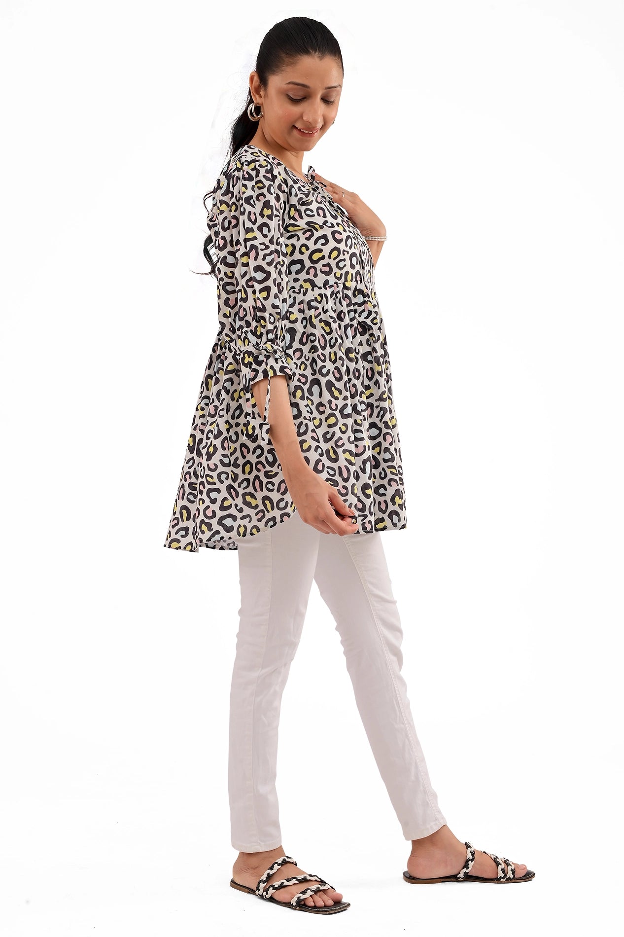 A model posing gracefully in a leopard print tunic, showcasing the trendy sleeve tie detail. The tunic has a loose silhouette, complementing the fitted white pants