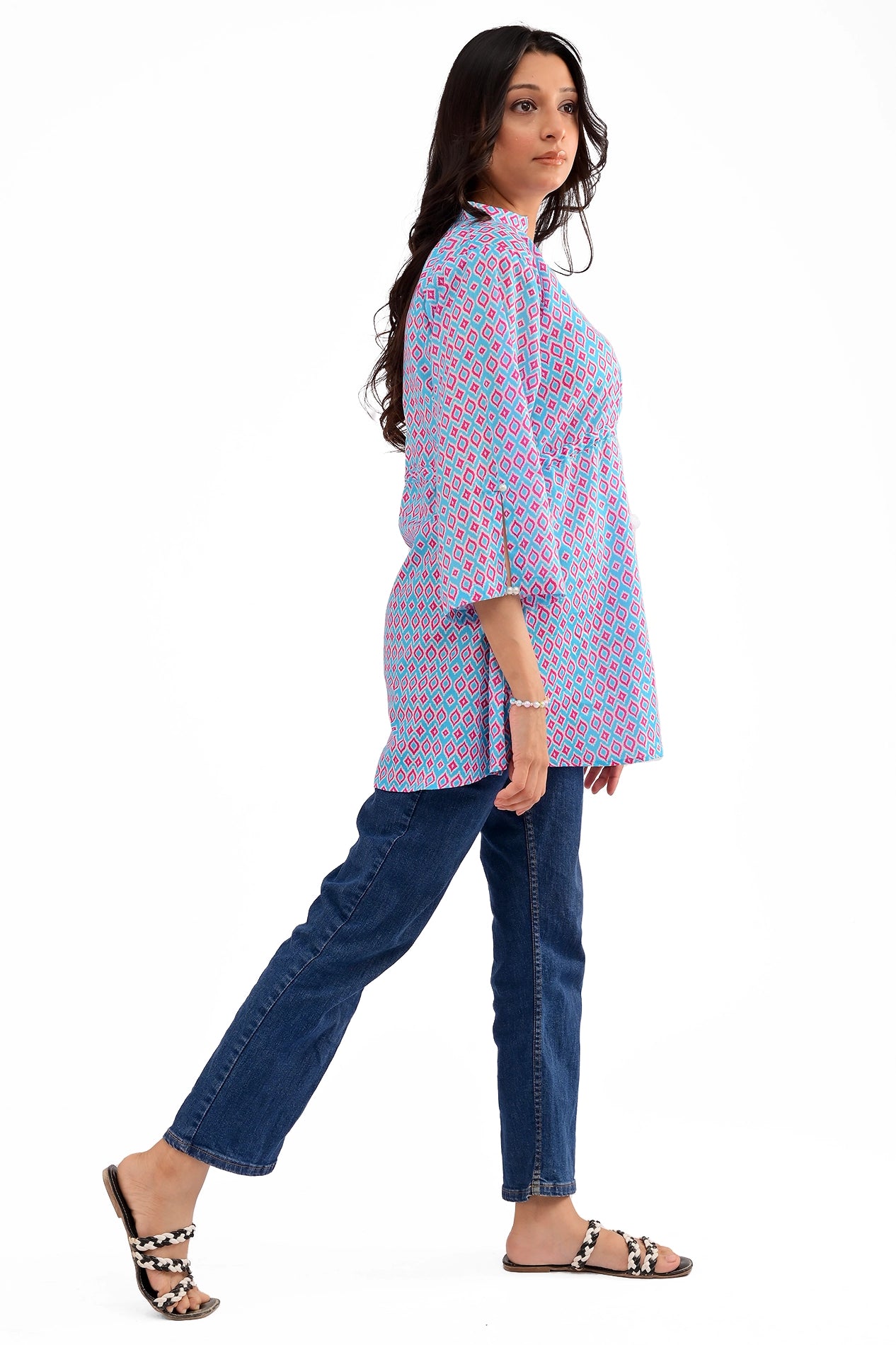Side view of a woman in a blue and pink geometric print tunic with flared sleeves and a cinched waist, styled with blue jeans
