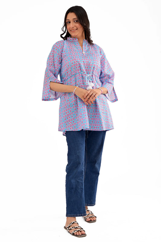 Woman wearing a blue and pink geometric print tunic with wide sleeves and a drawstring waist, paired with blue jeans and sandals