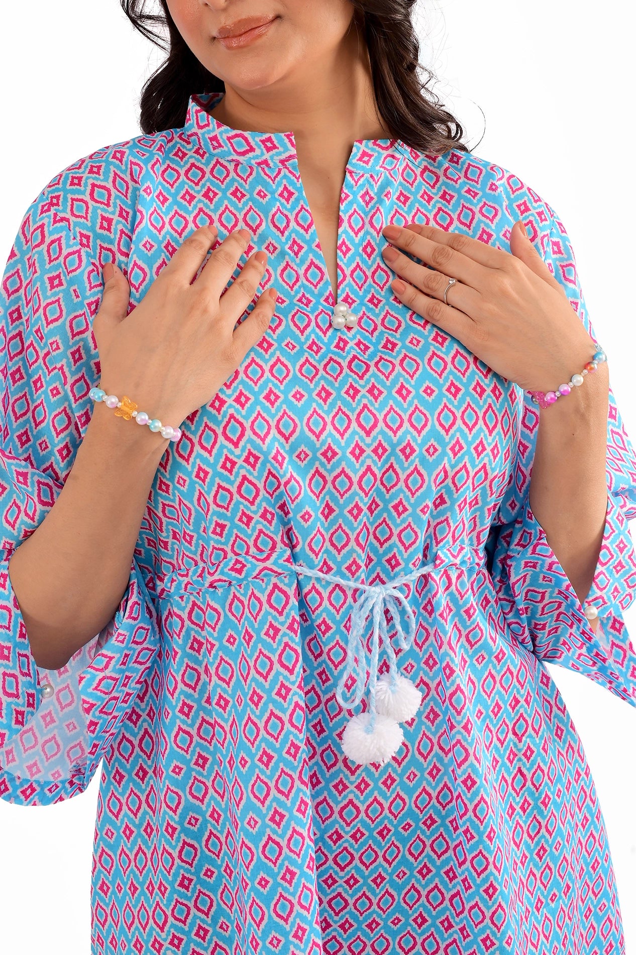 Close-up of a woman's upper body wearing a blue and pink geometric print tunic with a drawstring waist and pearl button details