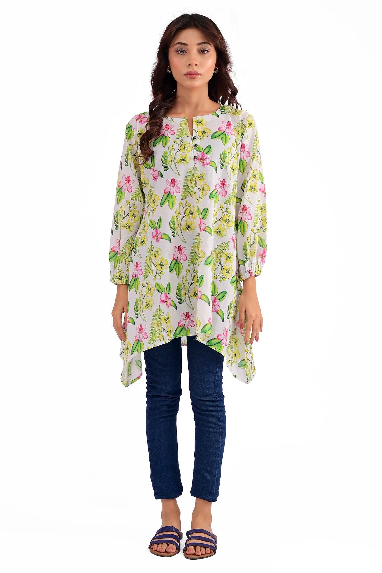 A model wearing a floral printed tunic with pink and yellow flowers on a white background, styled with blue jeans and casual sandals