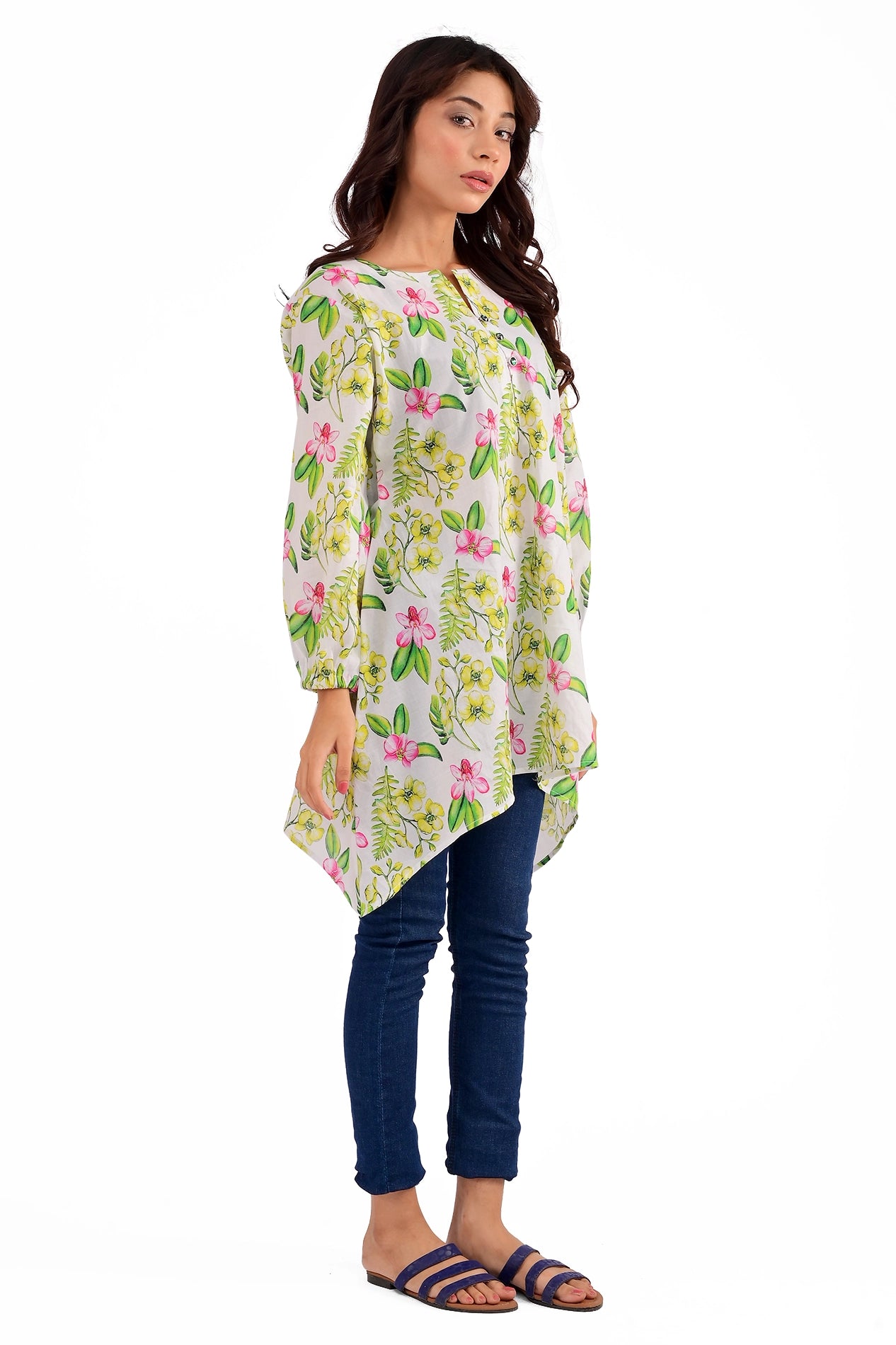 Side view of a model showcasing a vibrant floral printed tunic with asymmetrical hemline, paired with blue jeans