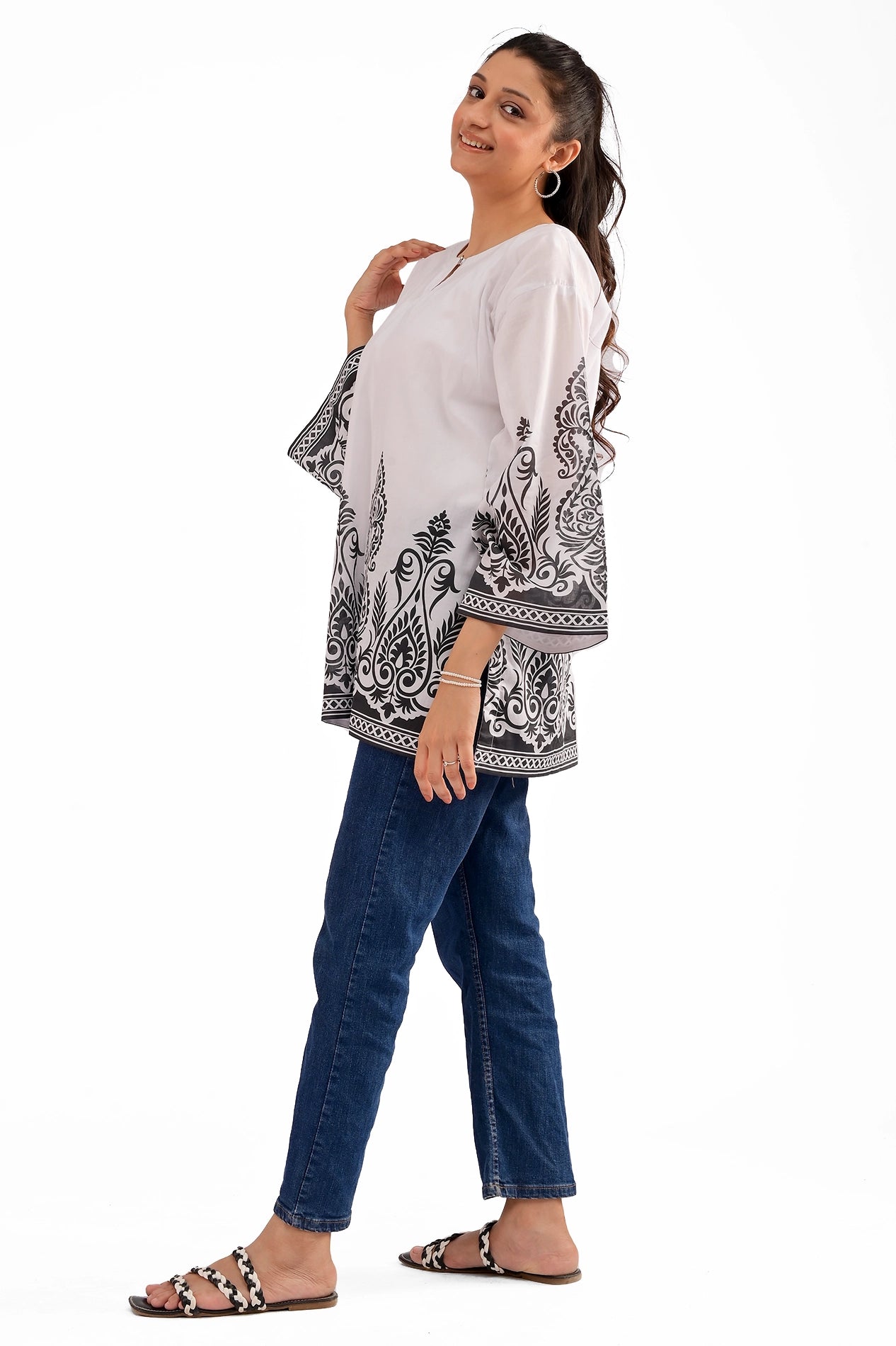 A model slightly turning sideways, showcasing the elegant flow of the white lawn kurti with its black ornamental border design