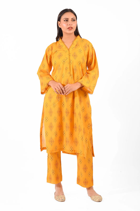 A model wearing a vibrant mustard yellow 2-piece dress. The shirt features intricate traditional patterns and lace details on the neckline and cuffs. Paired with straight pants of matching print, styled with woven khussa shoes. BOLDSTEP BOLDSTEP.PK