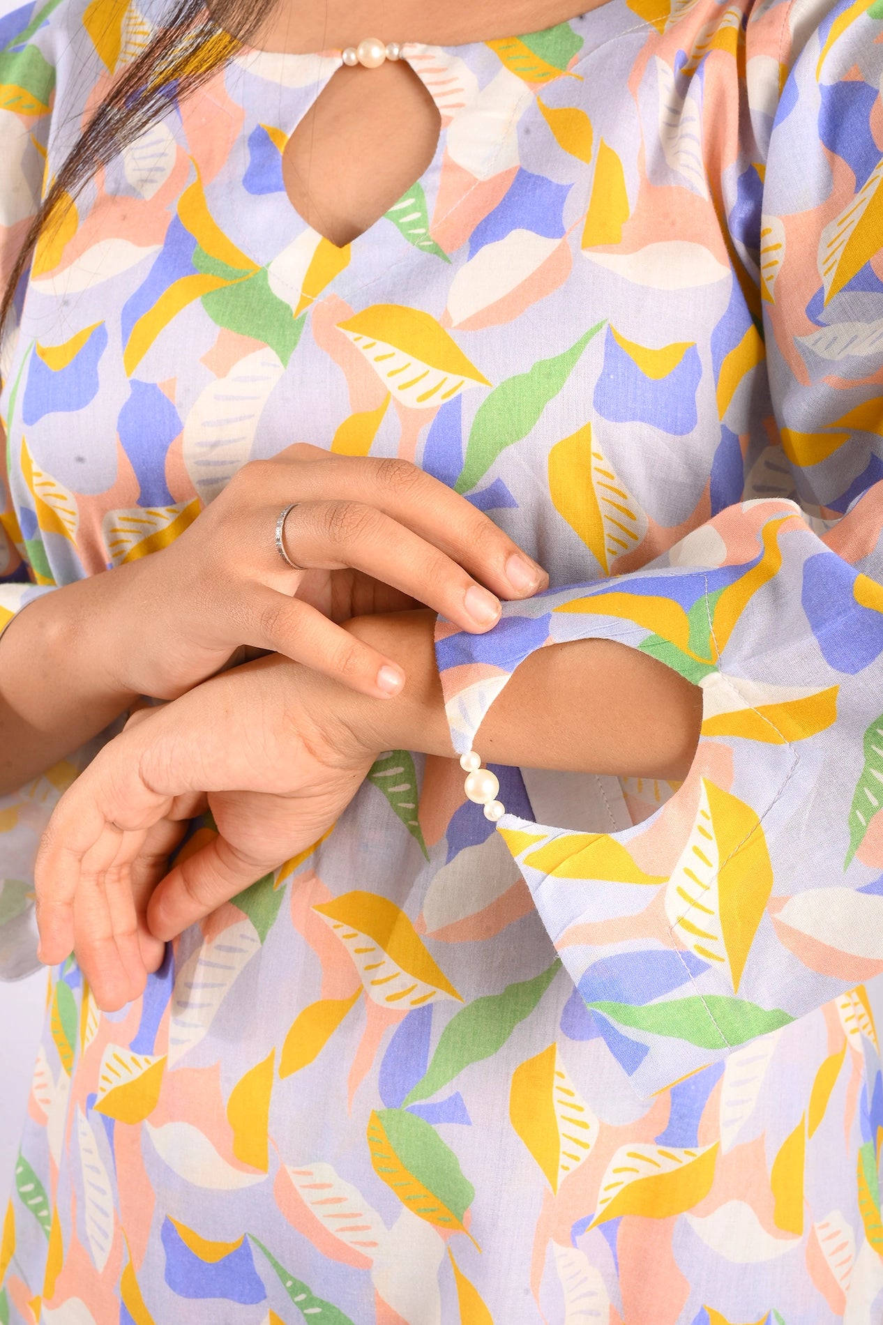 A close-up of the sleeves of a pastel-colored floral leaf patterned dress. The sleeves have a slit design, detailed with a pearl clasp, adding a touch of elegance and sophistication to the outfit BOLDSTEP BOLDSTEP.PK