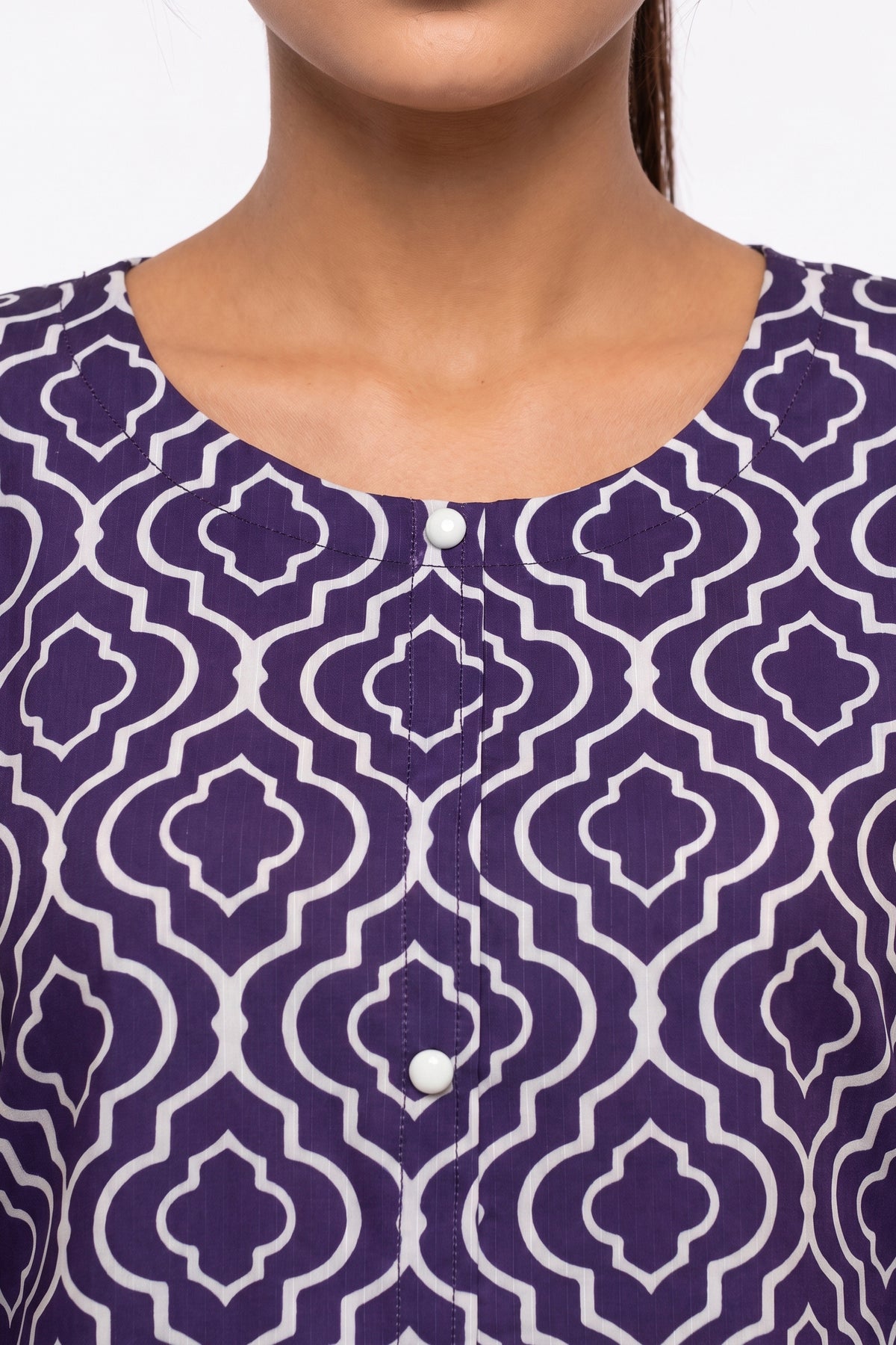 Close-up view of round neckline featuring white accent buttons on purple trellis print fabric.