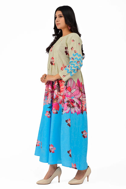 A side profile of the A-line dress showcasing its flowing fit and elegant pleats at the waistline. The off-white and sky blue dual-tone design is complemented by vibrant floral prints and zigzag patterns on the sleeves. BOLDSTEP BOLDSTEP.PK