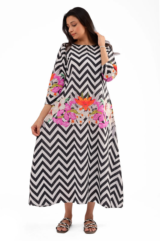 A woman wearing a black and white chevron-patterned cotton dress with vibrant floral digital prints on the sleeves and lower section. The dress has a round neckline and three-quarter sleeves.